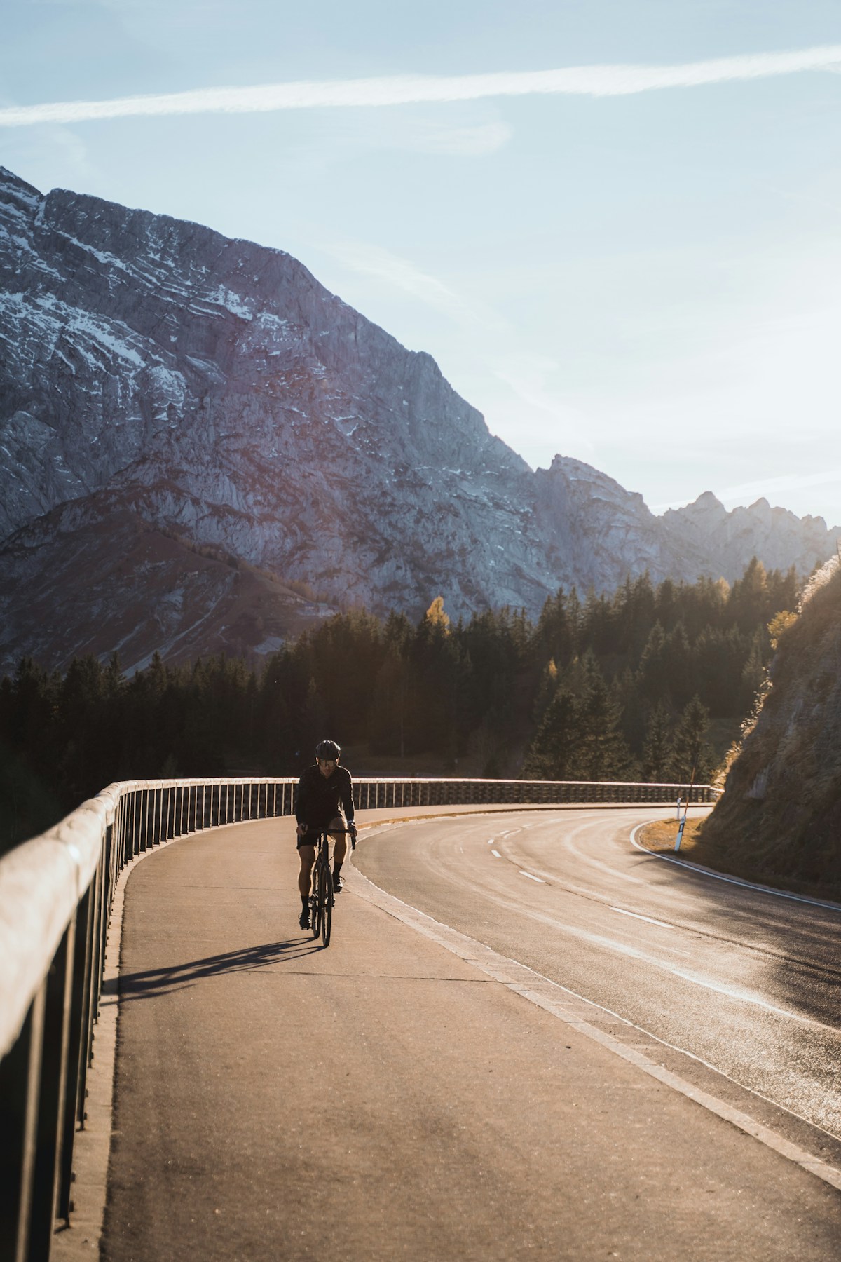 A cyclist riding along a mountain road with forest on either side