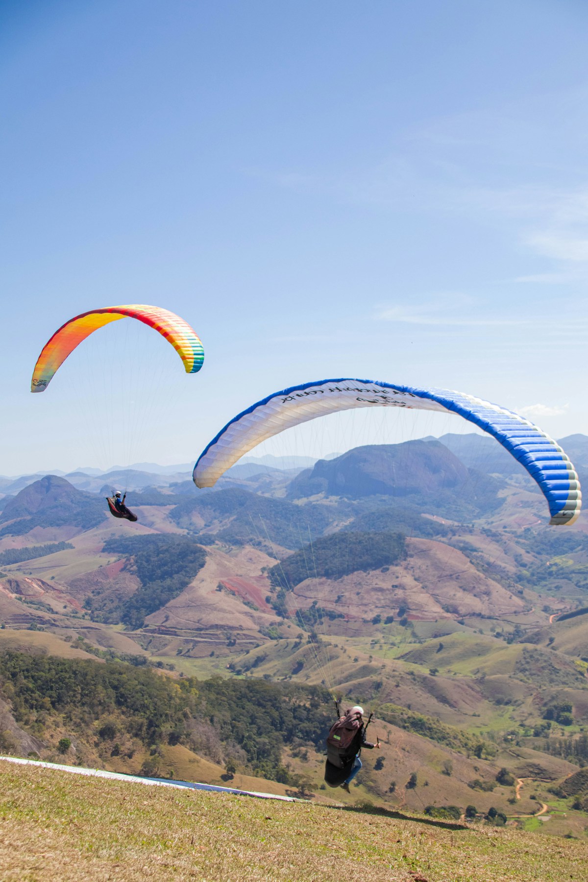 Two people paragliding over a mountain range on a clear day