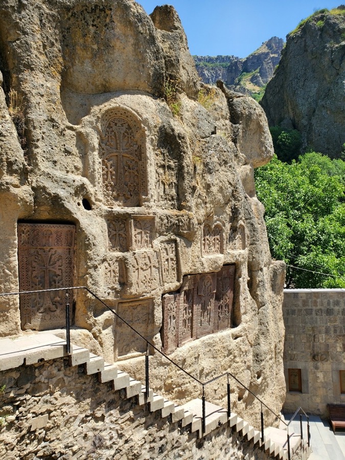 Khachkar cross-stones and ornate wooden doors carved into the rock face at Geghard Monastery, Armenia