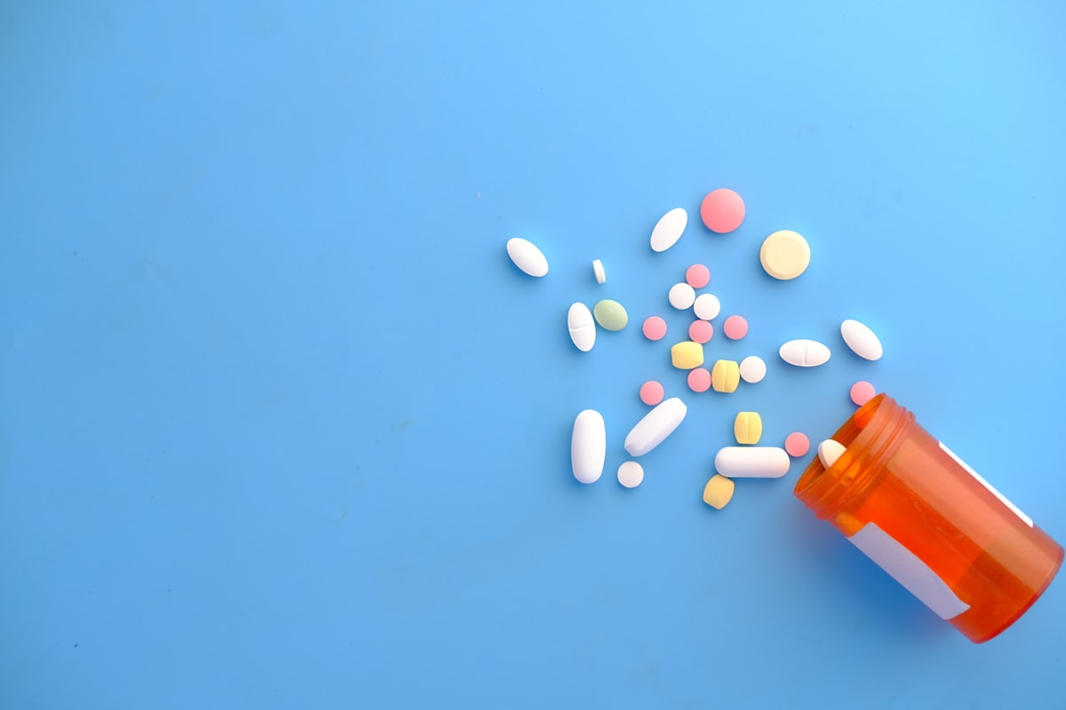 Prescription medication pills and capsules spilling from an orange medicine bottle